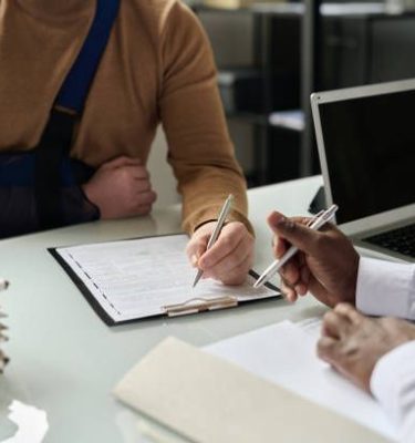 Close up of man filling in medical insurance form, injured hand in sling in background, copy space
